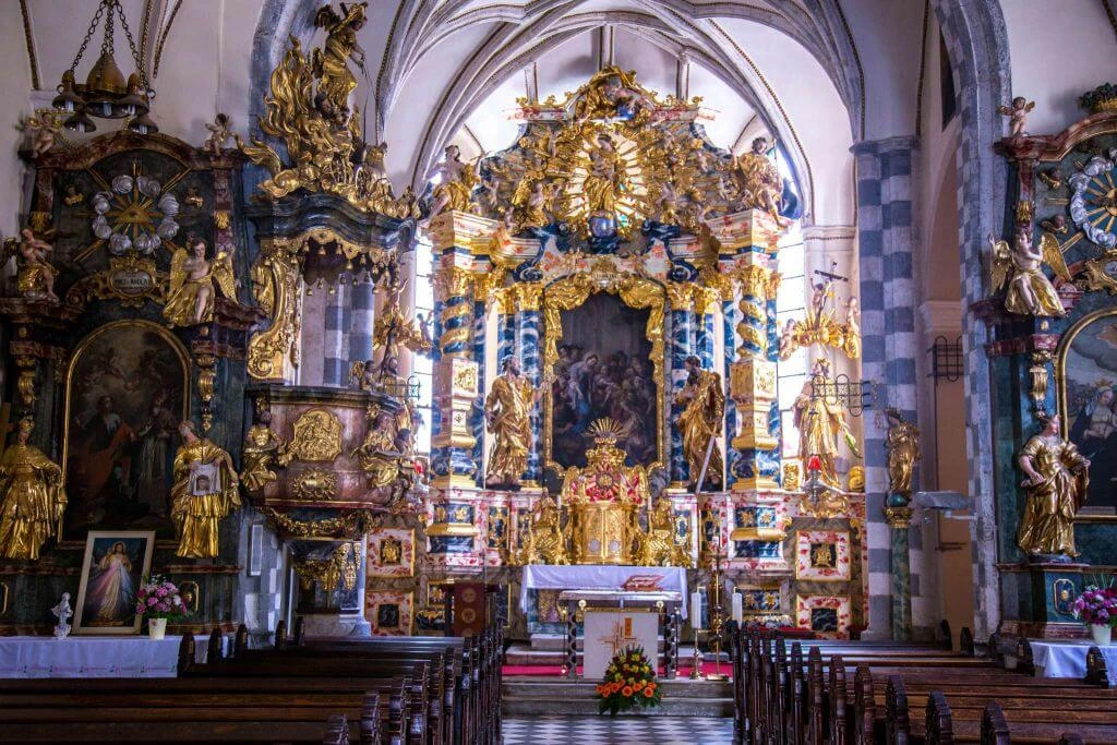 Überwältigend verzierter Barockkirchen-Innenraum mit goldenem Hochaltar, blauen Säulen und Holzbänken