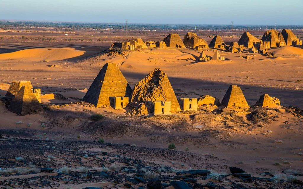 Antike Pyramidengruppe aus Ziegelsteinen in goldgelber Wüstenlandschaft, Sonnenlicht beleuchtet historische Architektur