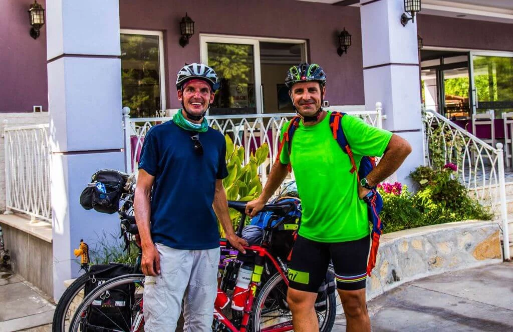 Zwei Männer in Fahrradkleidung mit Helm und Rädern vor einem Gebäude, einer in blauem, einer in grünem Shirt
