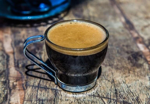 Schwarze Espressotasse mit goldbrauner Crema auf rustikaler Holzoberfläche