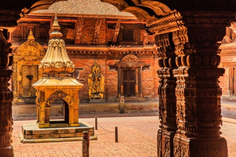 Goldverzierter Schrein mit Statuen und Säulen in einem alten Backsteingebäude mit traditioneller Nepalischer Architektur