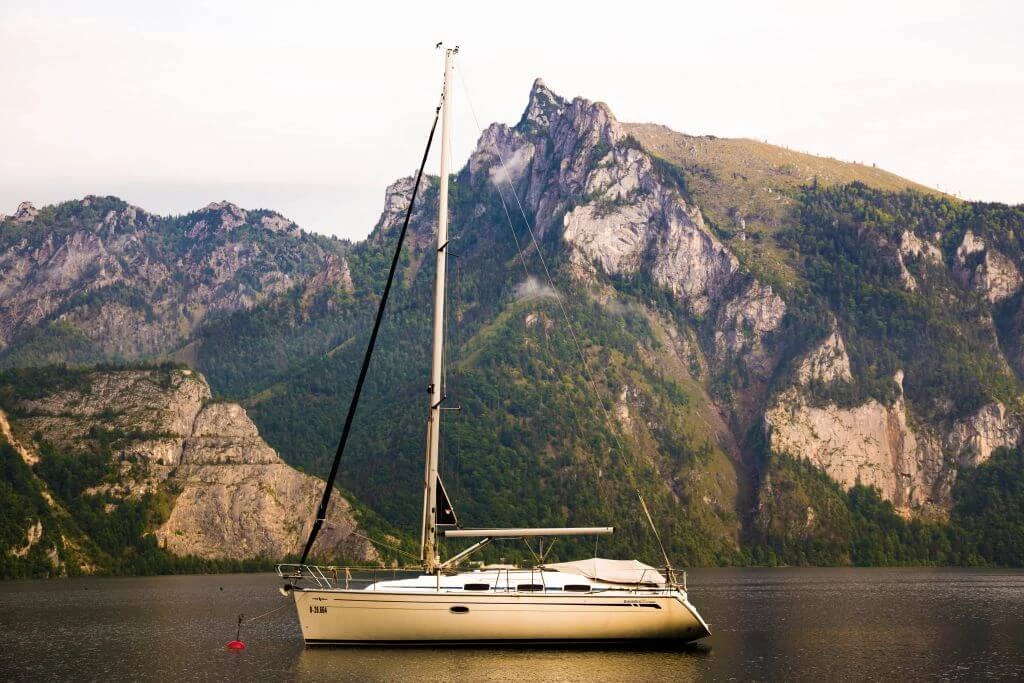 Weißes Segelboot auf ruhigem Bergsee, umgeben von steilen, felsigen Berghängen mit Wald
