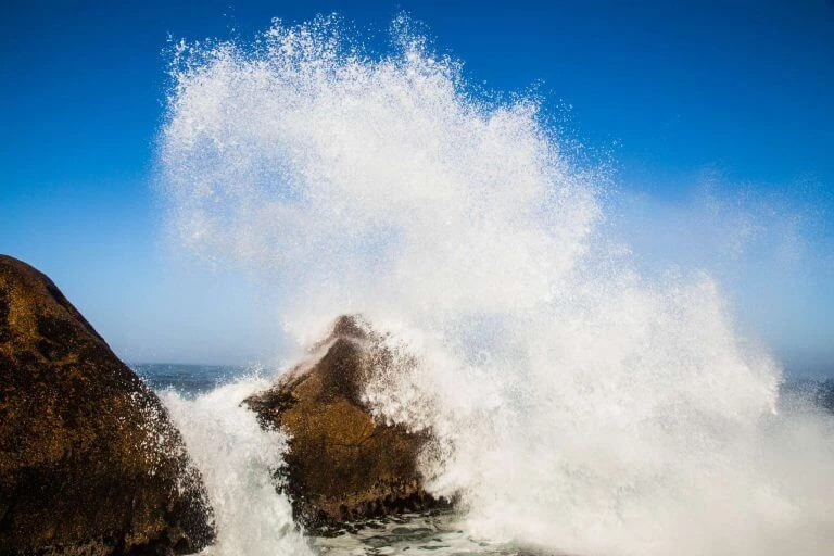 Große weiße Gischt und Wasserspray einer stürmischen Meereswelle, die gegen einen braunen Felsen spritzt