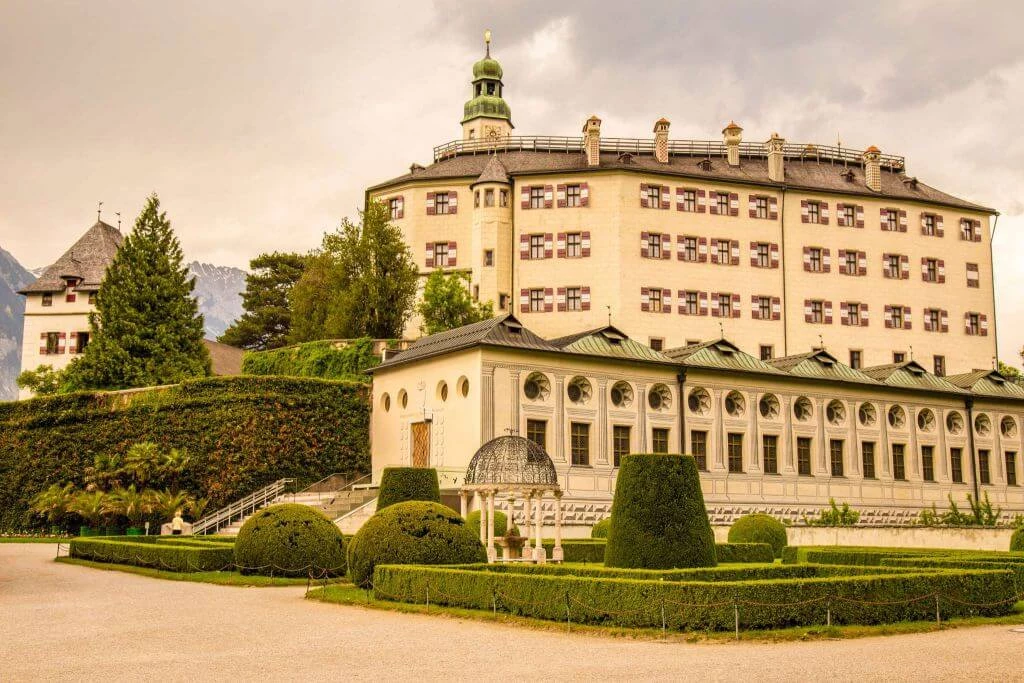 Barockes Schloss mit grünem Turm, umgeben von geometrischen Gärten und Bergen im Hintergrund