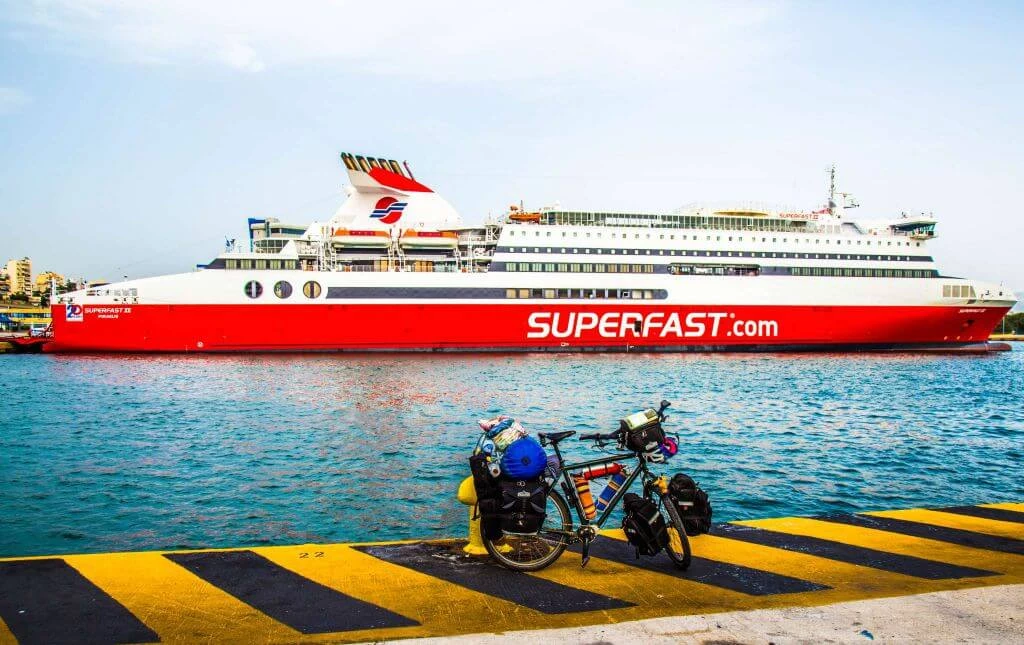 Beladenes Fahrrad auf gelbschwarz gestreifter Hafenrampe mit rotem Passagierschiff im Hintergrund