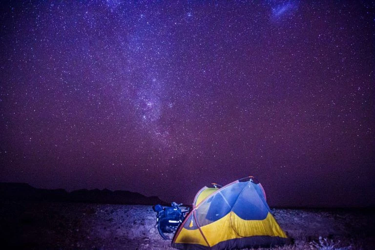 Leuchtendes gelb-blaues Zelt unter einem atemberaubend klaren, sternenübersäten Nachthimmel mit Milchstraße