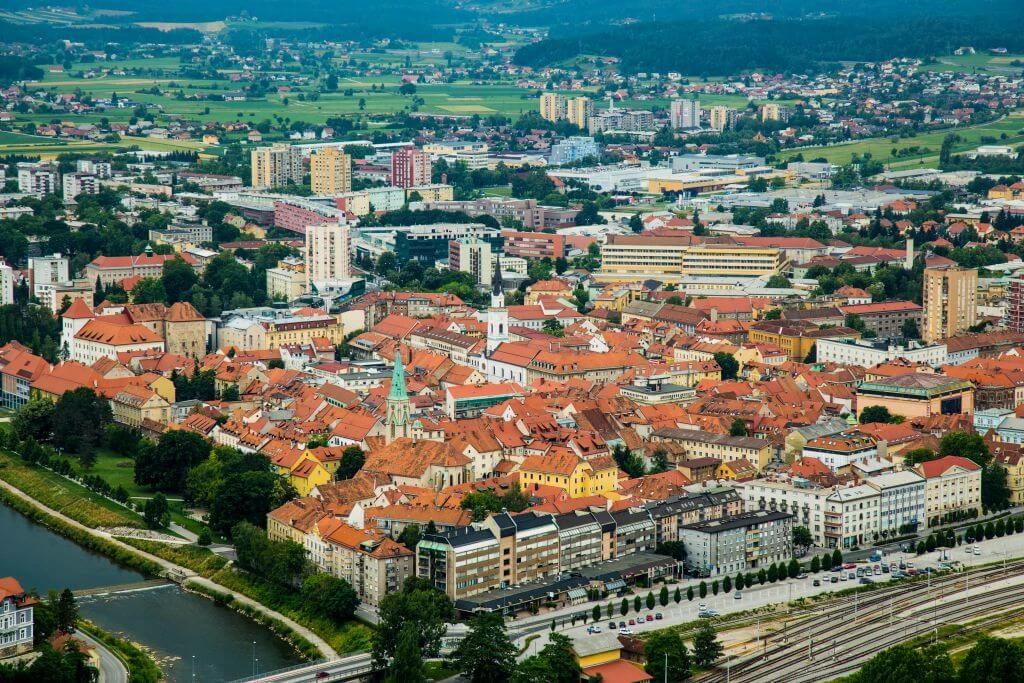 Panoramic view of a Slovenian city with red-roofed historic center, modern buildings, and green surroundings