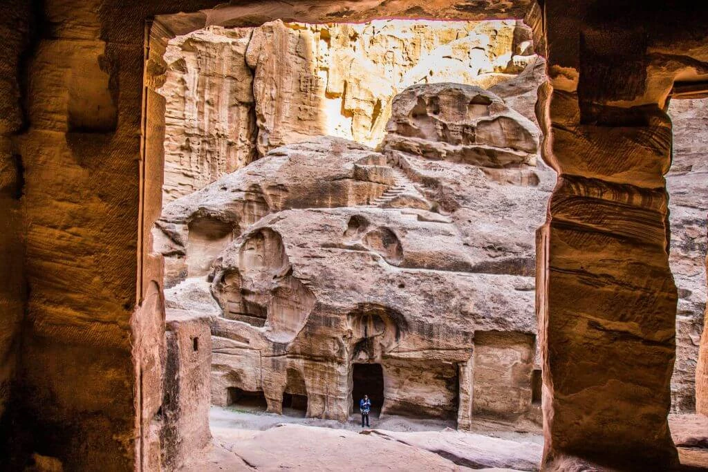 Blick durch steinernes Felsentor auf mehrere ausgehöhlte Etagen und Nischen in beige-brauner Felsenlandschaft mit einer Person im Eingang