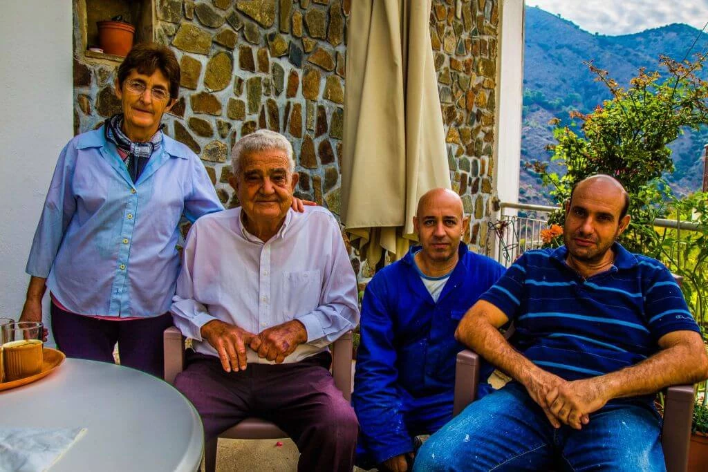 Vier Menschen unterschiedlichen Alters sitzen auf einer Terrasse mit Natursteinwand und Bergpanorama im Hintergrund