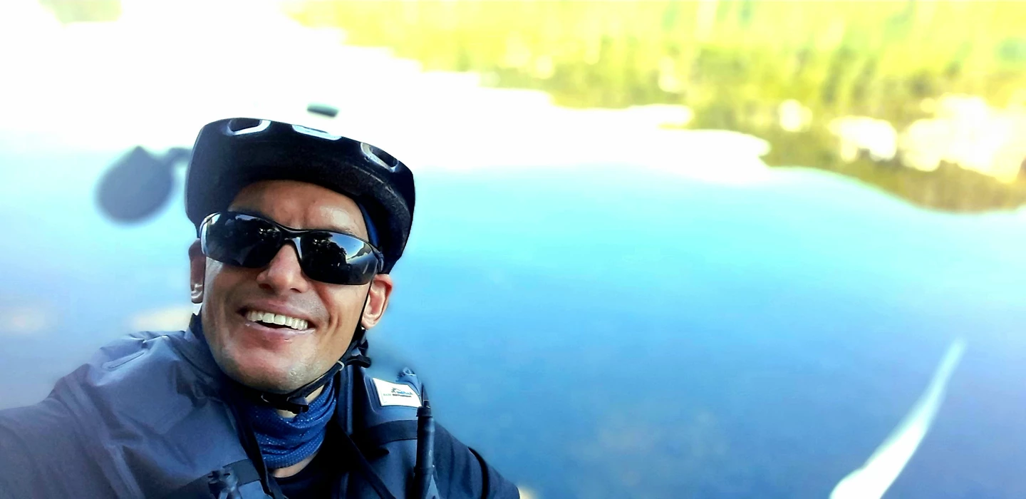 Lächelnder Radfahrer mit Helm, Sonnenbrille und blauer Jacke vor blauem Hintergrund