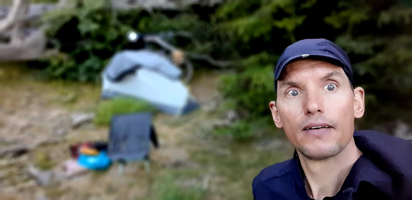 Person mit blauer Kappe schaut überrascht in die Kamera, im Hintergrund Vegetation und unscharfe Gegenstände