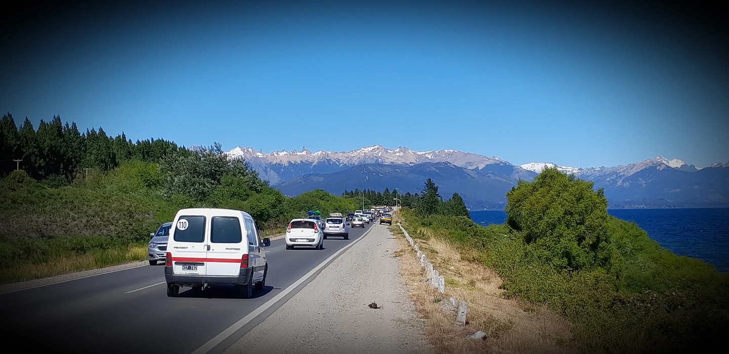 Asphaltierte Landstraße mit Autos, Blick auf schneebedeckte Berge, grüne Vegetation und blauen See