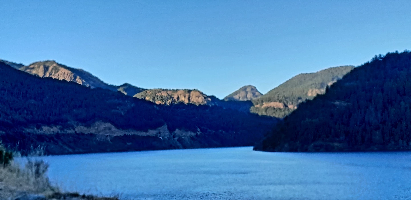 Stiller See mit blauem Wasser, umgeben von dunklen Bergketten mit felsigen Gipfeln und Nadelwäldern