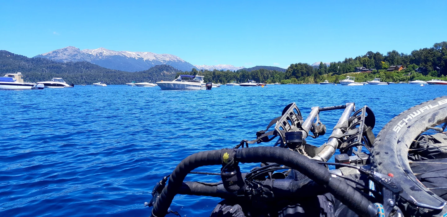 Blick auf einen blauen See mit mehreren weißen Motorbooten, im Hintergrund verschneite Berge und Wälder