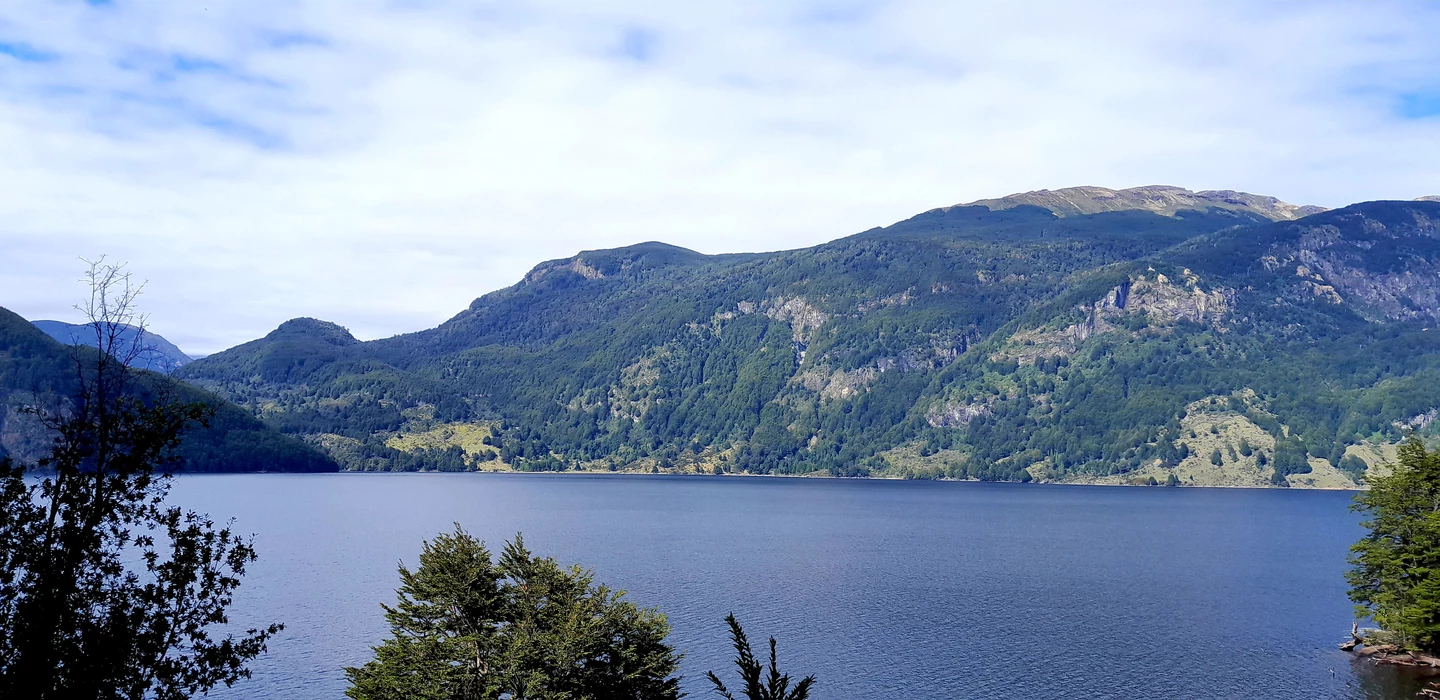 Weiter blauer See umgeben von dicht bewaldeten Berghängen in Patagonien, grüne Landschaft mit felsigen Bergkämmen