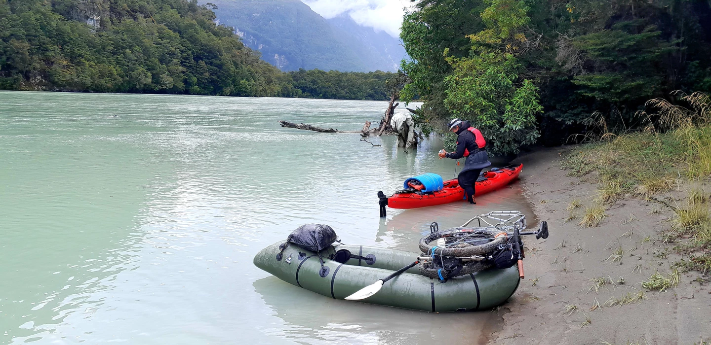 Zwei Packrafts an sandiger Flussufer mit Gebirge, grün-blau schimmerndes Wasser, Bäume und Berge im Hintergrund
