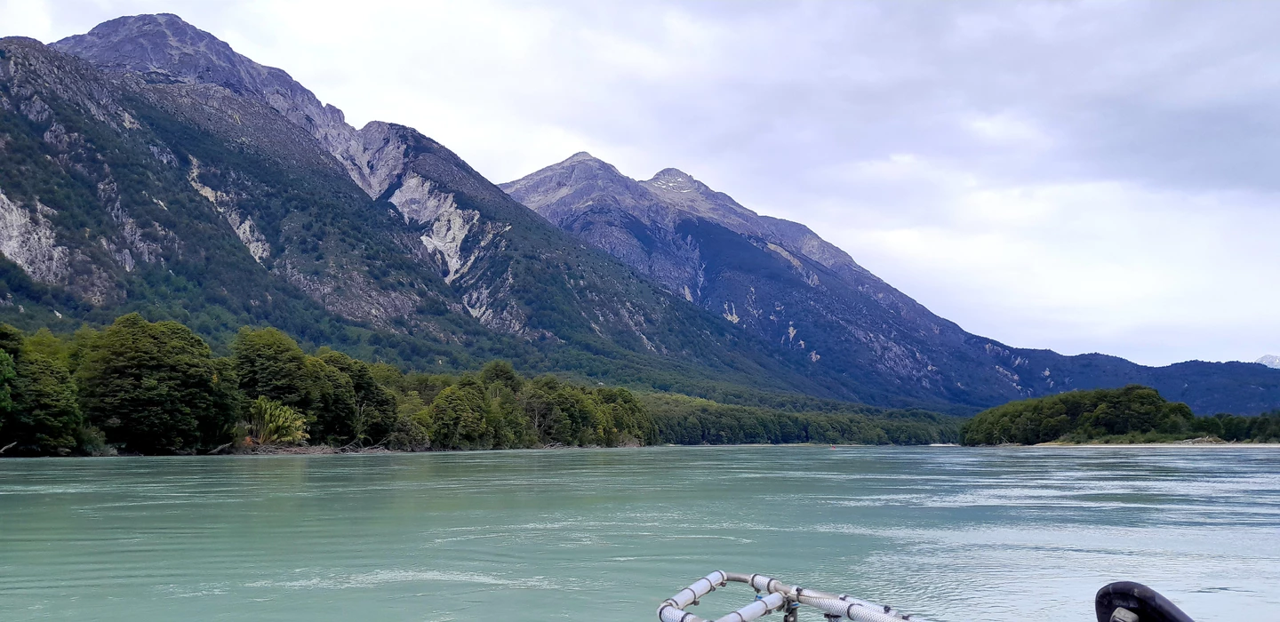 Türkisfarbener Fluss mit dicht bewaldeten Ufern, umgeben von hohen, felsigen Bergen unter bewölktem Himmel