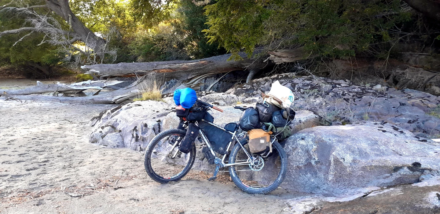 Zwei beladene Mountainbikes auf großen Granitfelsen, Hintergrund Baumstämme und Geröll, raue Flusslandschaft