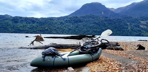 Grünes Packraft am Ufer eines Sees, umgeben von bewaldeten Bergen und Felsbrocken