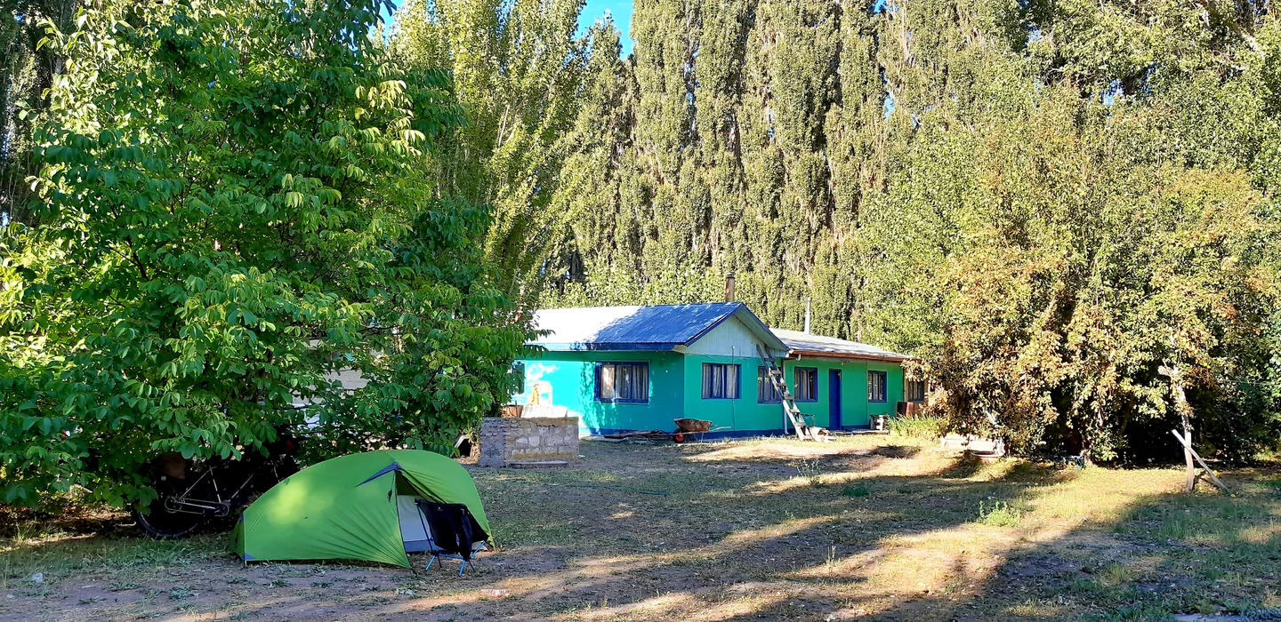 Türkisfarbenes Holzhaus mit blauem Wellblechdach, daneben ein hellgrünes Zelt in ländlicher Waldumgebung