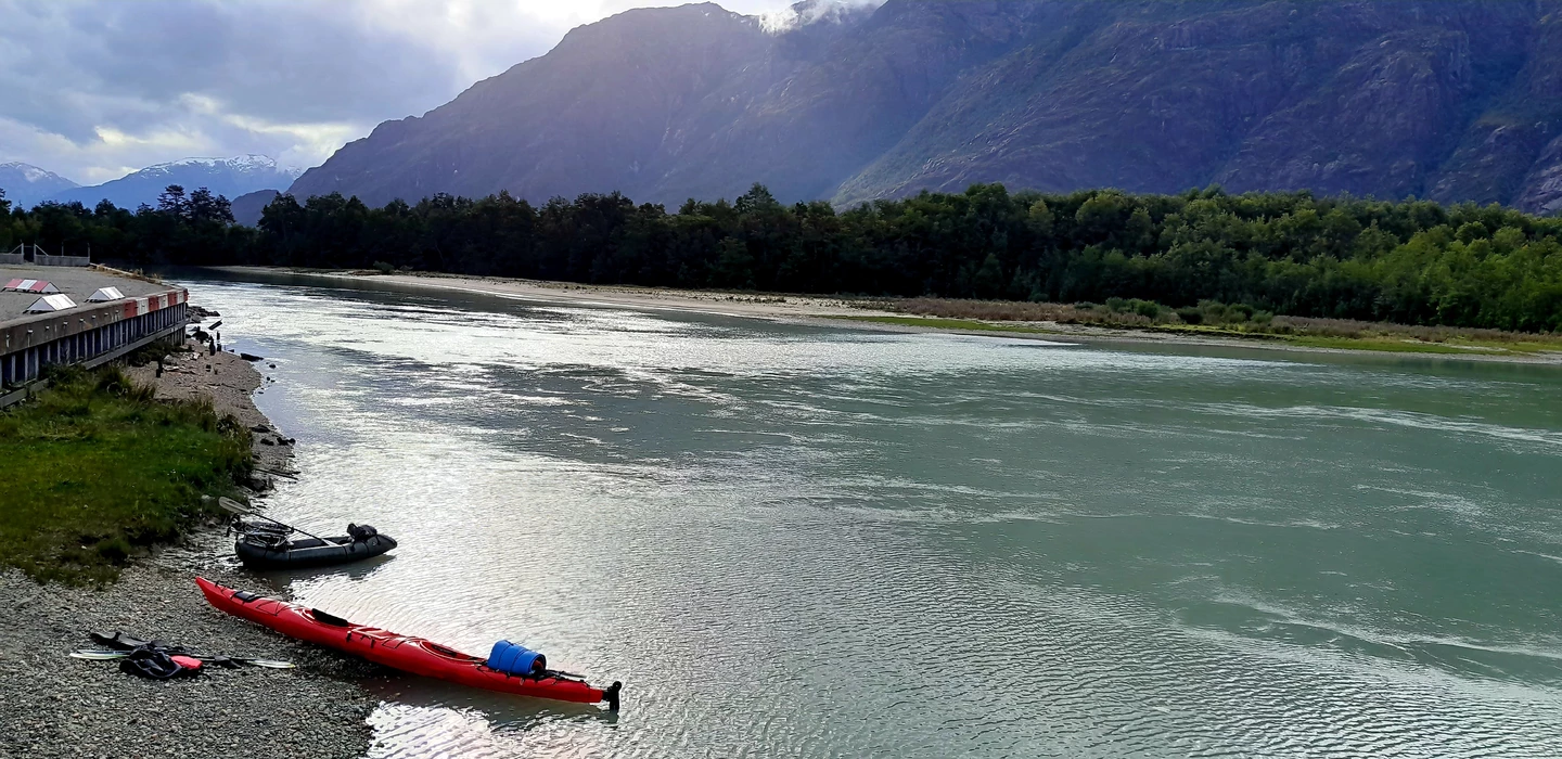 Rot-schwarzer Kajak am Ufer eines türkisfarbenen Gletscherflusses, umgeben von Bergen und Wäldern in Patagonien