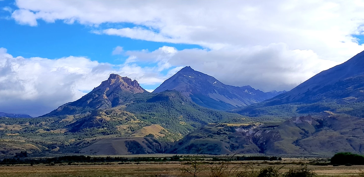 Weite Berglandschaft mit markanten Gipfeln, Wäldern und Grasebenen in Patagonien, blauer Himmel