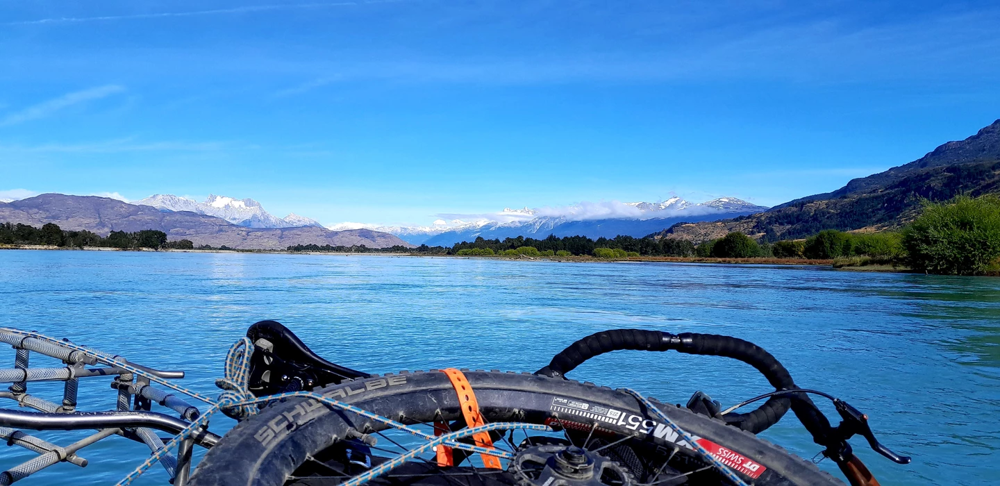 Fahrradlenker mit Seilbefestigungen vor blauem Gebirgssee, Schneeberge im Hintergrund, weite Landschaft