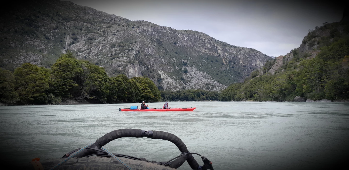 Zwei rote Kajaks auf einem grauen See, umgeben von bewaldeten Bergen und felsigen Bergketten in Patagonien
