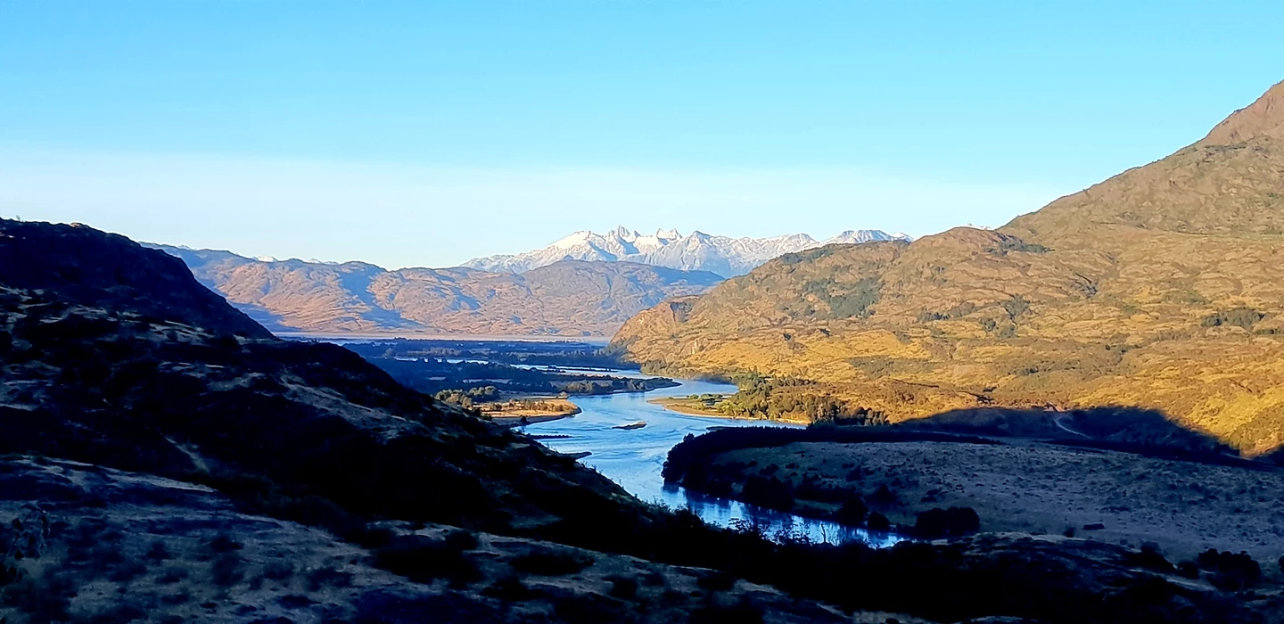 Weite Berglandschaft mit blauem Fluss, schneebedeckten Gipfeln und herbstlich-braunen Hängen in Patagonien