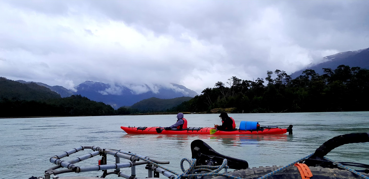 Zwei Kayaker in roten Booten auf einem Fluss, umgeben von nebligen Bergen, Wäldern und wolkenverhangener Landschaft