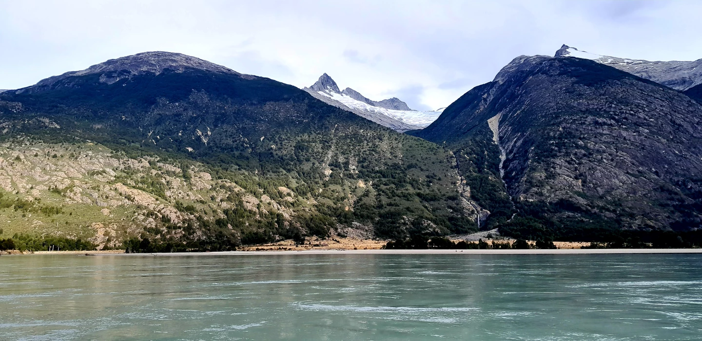 Weite Berglandschaft mit schneebedeckten Gipfeln, grünem Wald und türkisfarbenem See im Vordergrund