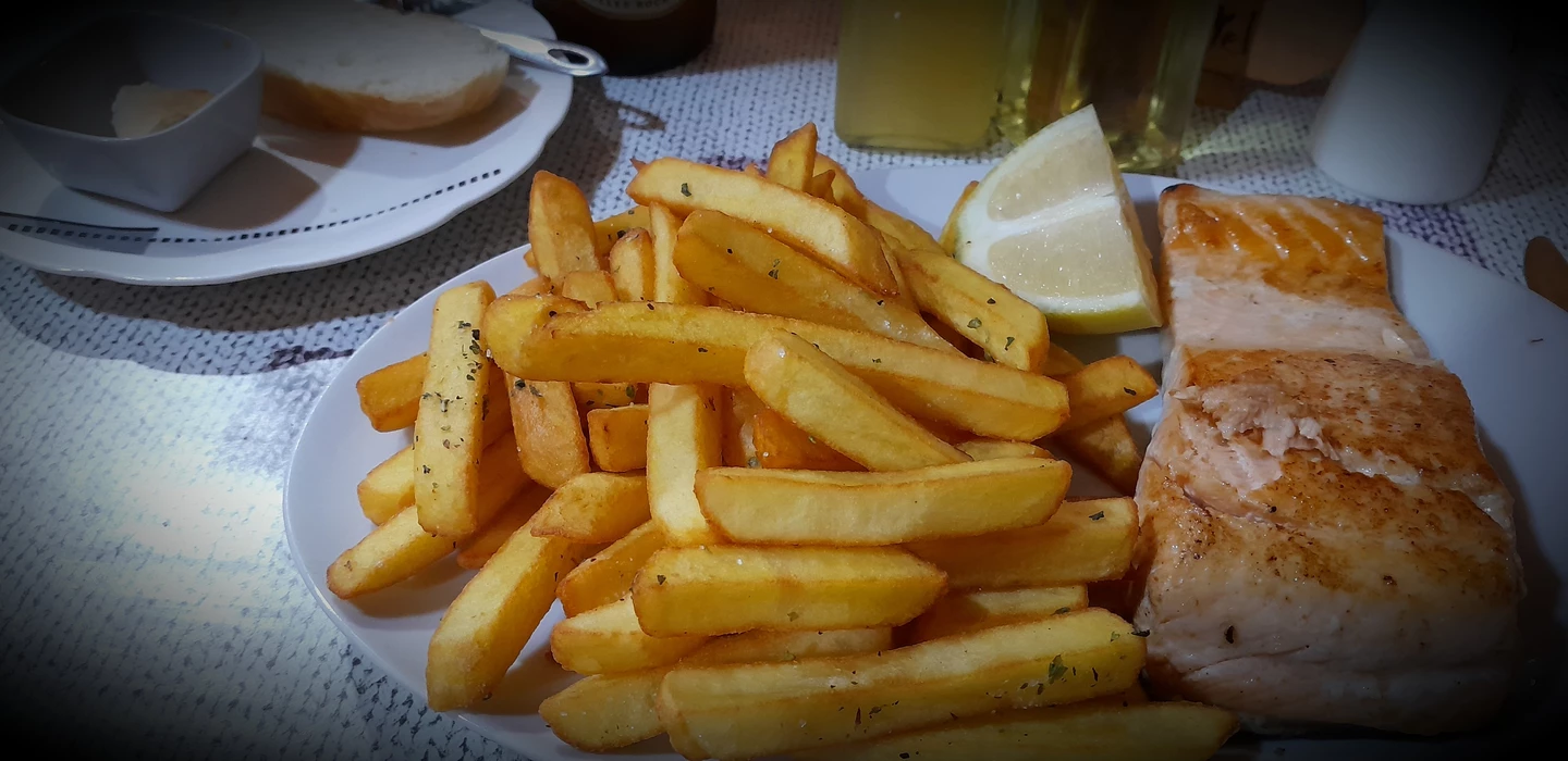 Gebratenes Lachsfilet auf weißem Teller, daneben goldgelbe Pommes frites und ein Zitronenschnitz
