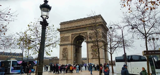 Berühmtes Pariser Wahrzeichen Arc de Triomphe an bewölktem Herbsttag mit kahlen Bäumen und Besuchergruppen