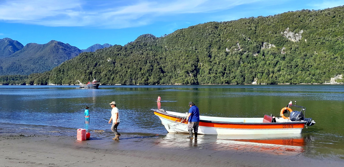 Orangeweißes Motorboot am Strand, dahinter grüne Berge und blauer See mit Berglandschaft in Patagonien