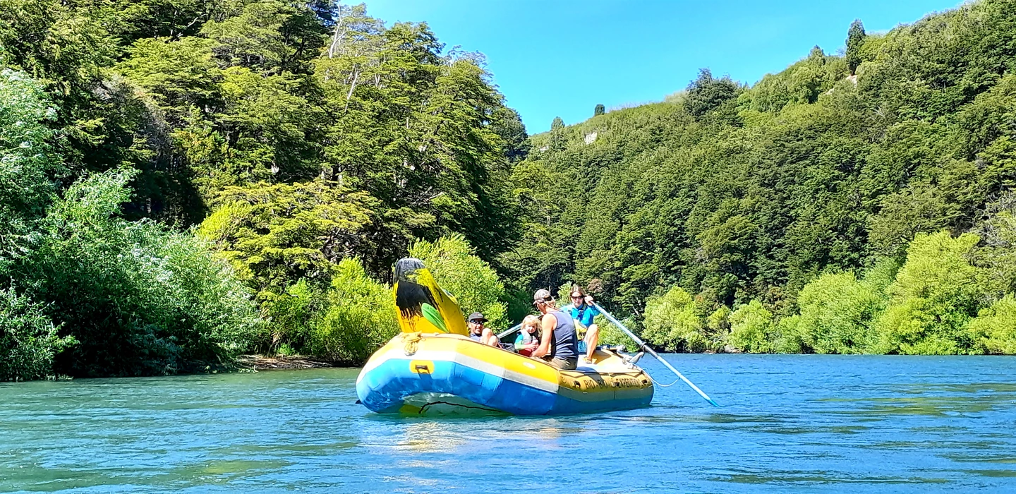 Gelbes und blaues Schlauchboot mit Personen auf grün bewachsenem Fluss, umgeben von dichten Wäldern