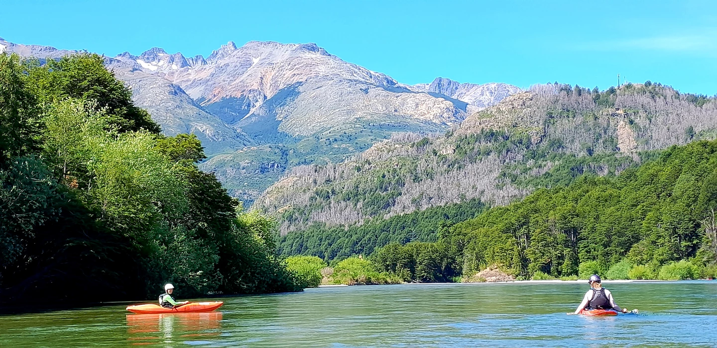 Zwei Kajakfahrer paddeln auf grünblauem Fluss, umgeben von dichten Wäldern und hohen Bergketten der Patagonischen Anden