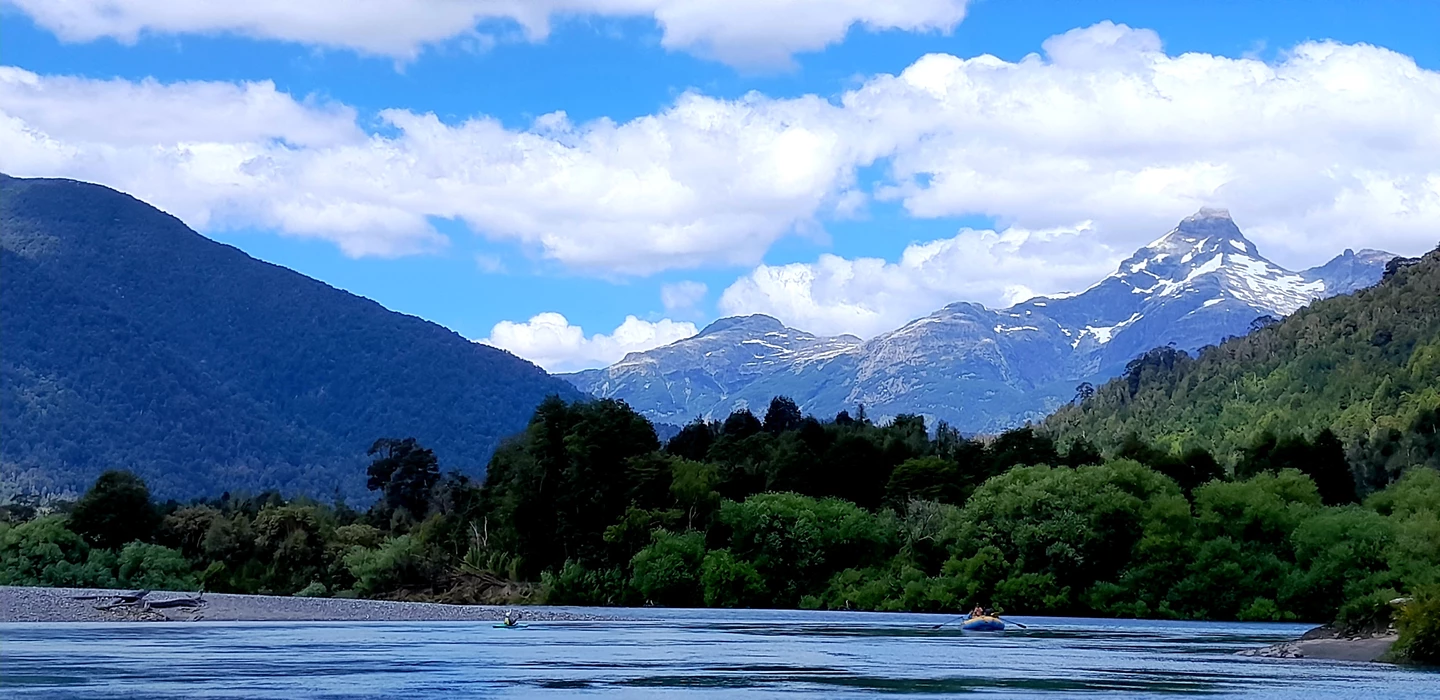Blick auf einen blauen Fluss mit Kajak, umgeben von grünen Wäldern und schneebedeckten Bergen in Patagonien