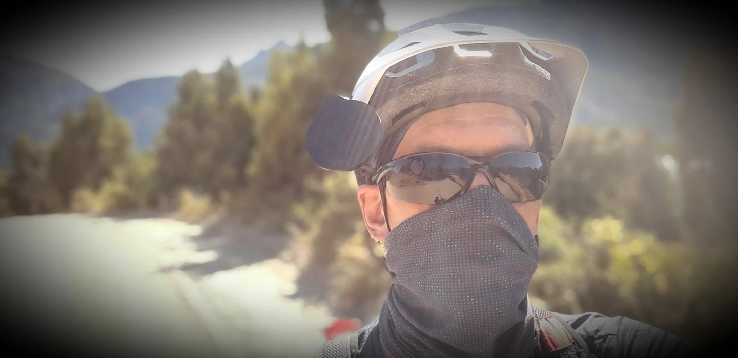 Radfahrer mit Fahrradhelm, Sonnenbrille und Mundschutz vor Berglandschaft mit Bäumen und Nebel