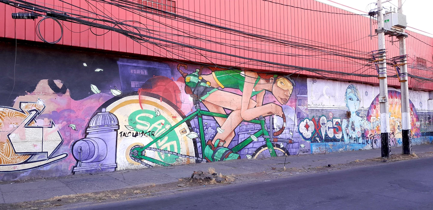 Buntes Wandgemälde mit Radfahrer auf grünem Fahrrad, umgeben von Straßenkunst und Stromleitungen