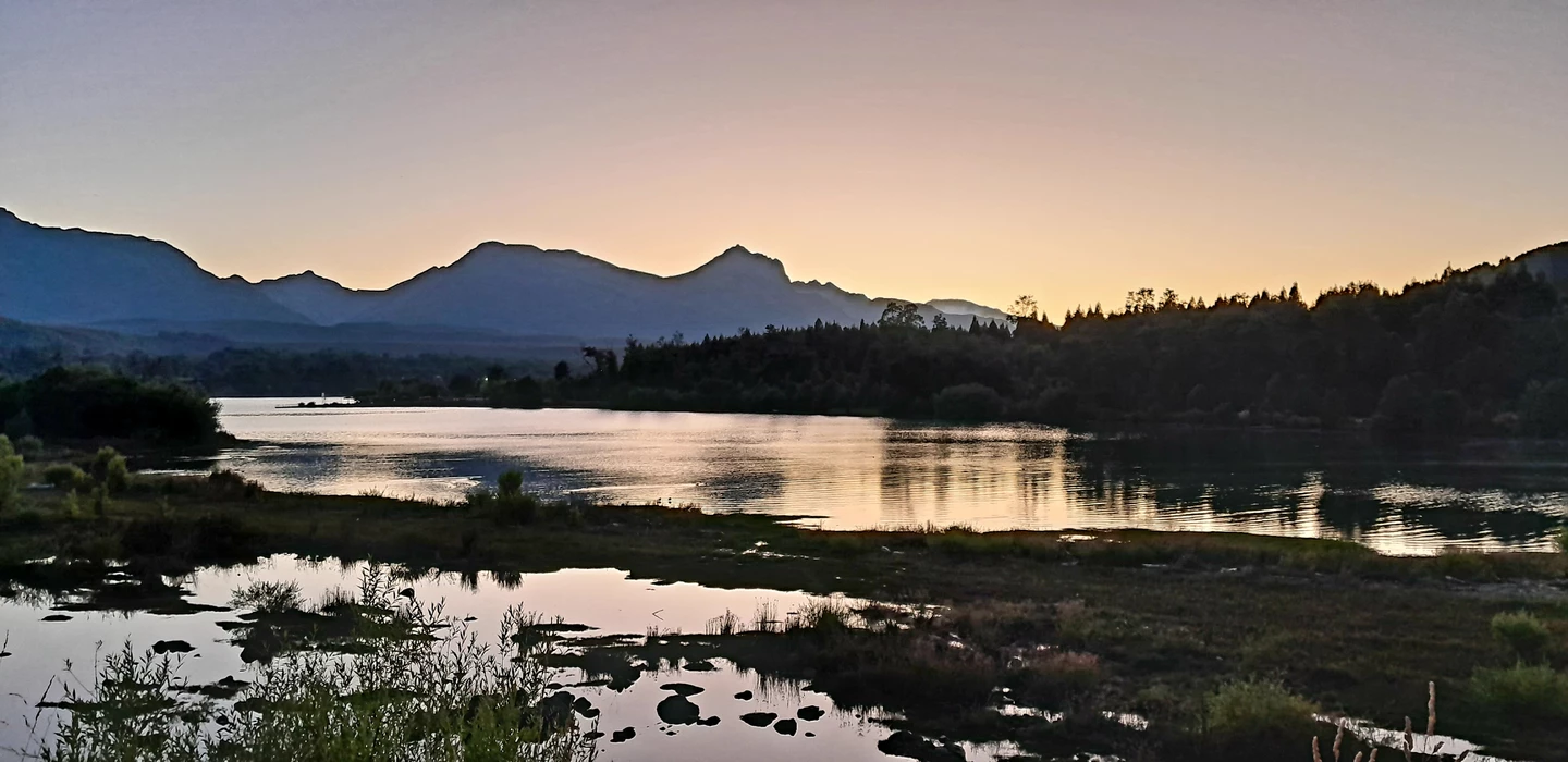 Weite Landschaft mit spiegelblankem See, Kiefernwald und Bergsilhouetten im warmen Abendlicht
