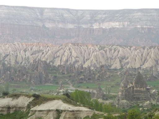 Bizarre Felsenformation mit zerklüfteten Steinpyramiden, grünen Tälern und Bergkulisse in Kappadokien, Türkei