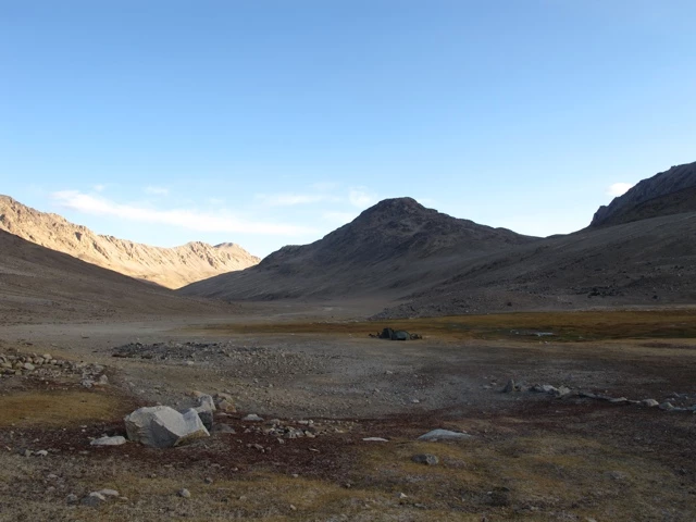 Weite Hochebene mit steiniger Landschaft, umgeben von braunen Bergketten unter blauem Himmel, felsiges Terrain mit spärlicher Vegetation
