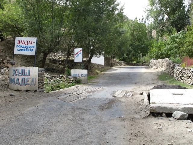 Schmaler Schotterweg zwischen Steinmauern und Bäumen, mit Verkehrsschildern und unebener Wegoberfläche