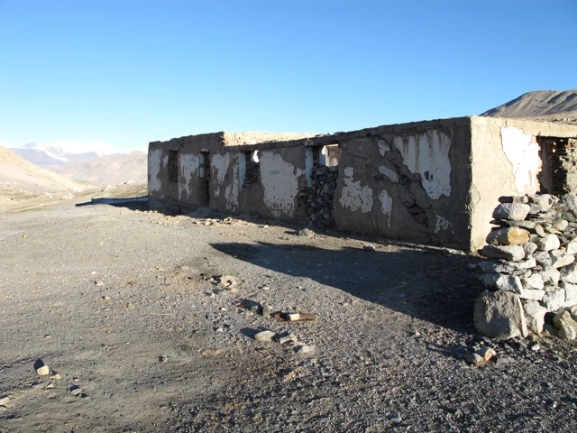 Alte, verwitterte Steinmauer mit Löchern in karger Berglandschaft mit steinigem Boden und blauem Himmel