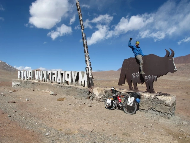 Fahrradtour in karger Hochebene des Atacama. Metallener Ochse, Fahrrad mit Satteltaschen, Wegweiser und Person auf 4.655 Metern über Meer