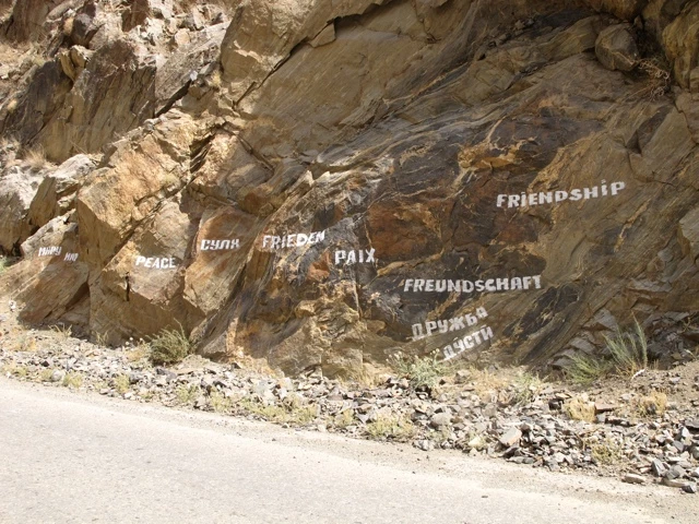 Felswand an einer Straße mit mehrfach beschrifteten Wörtern wie 'Peace', 'Frieden', 'Friendship' in verschiedenen Sprachen