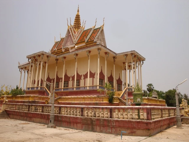 Goldverzierter traditioneller kambodschanischer Palast mit spitzen Dächern, weißen Säulen und roter Sockelzone