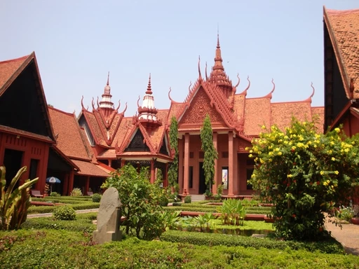 Traditionelles kambodschanisches Gebäude mit roten Ziegeldächern und geschwungenen Giebeln, umgeben von einem grünen Garten mit Büschen und Bäumen