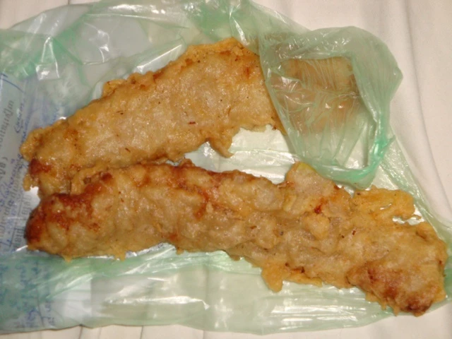 Zwei goldbraun frittierte, knusprige Fischfilets auf einer grünlichen Plastiktüte liegend