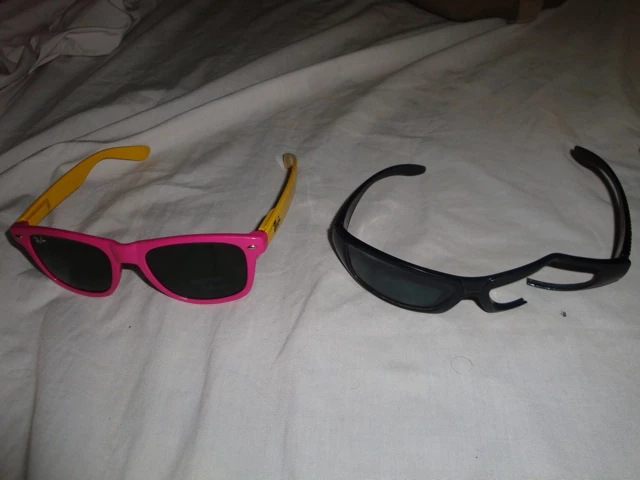 Eine pinke und gelbe Sonnenbrille neben einer schwarzen Sonnenbrille auf einem grauen Textiluntergrund